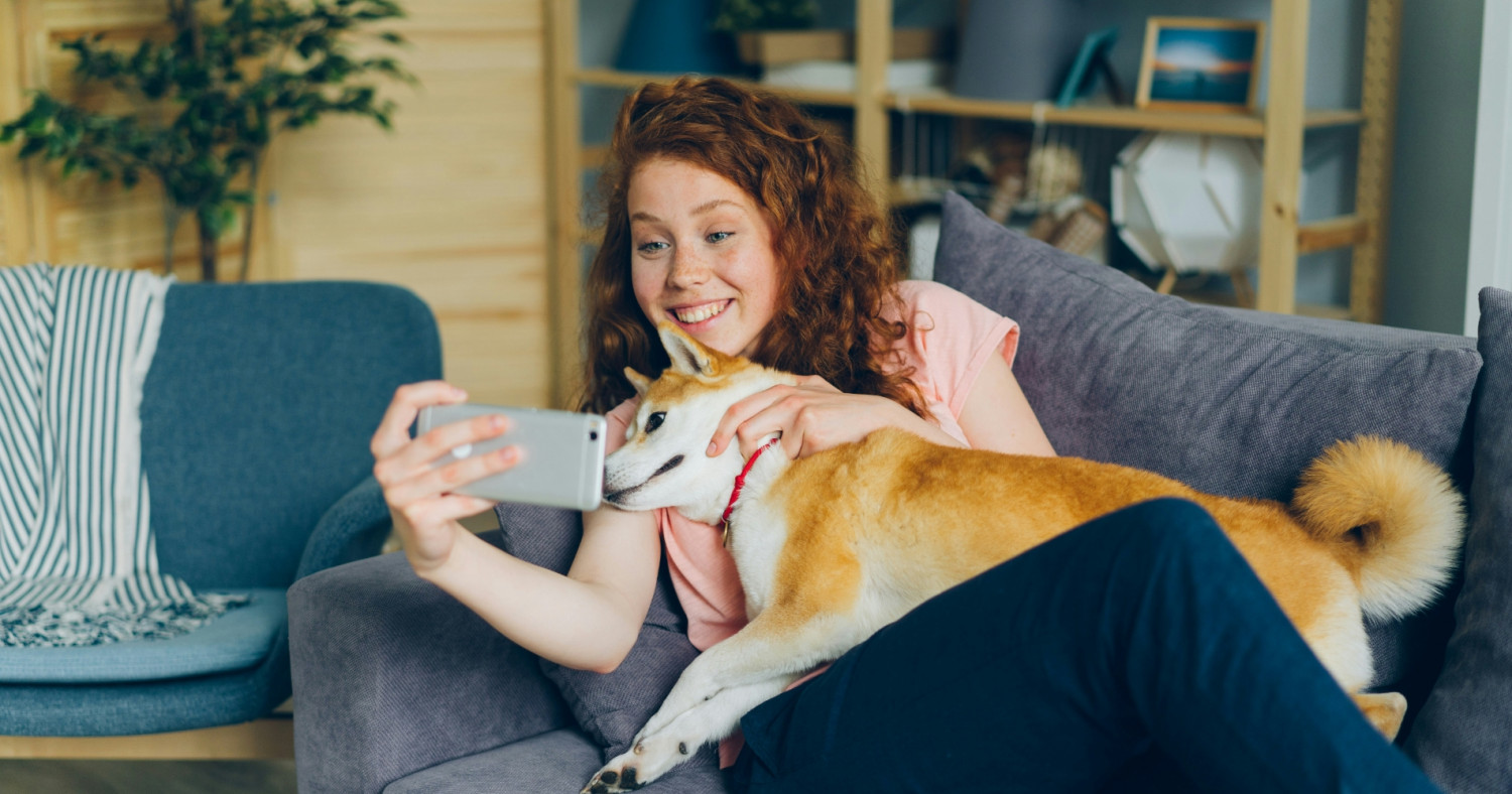 Eine junge Frau liegt mit einem Hund auf einer Couch und filmt sich dabei.
