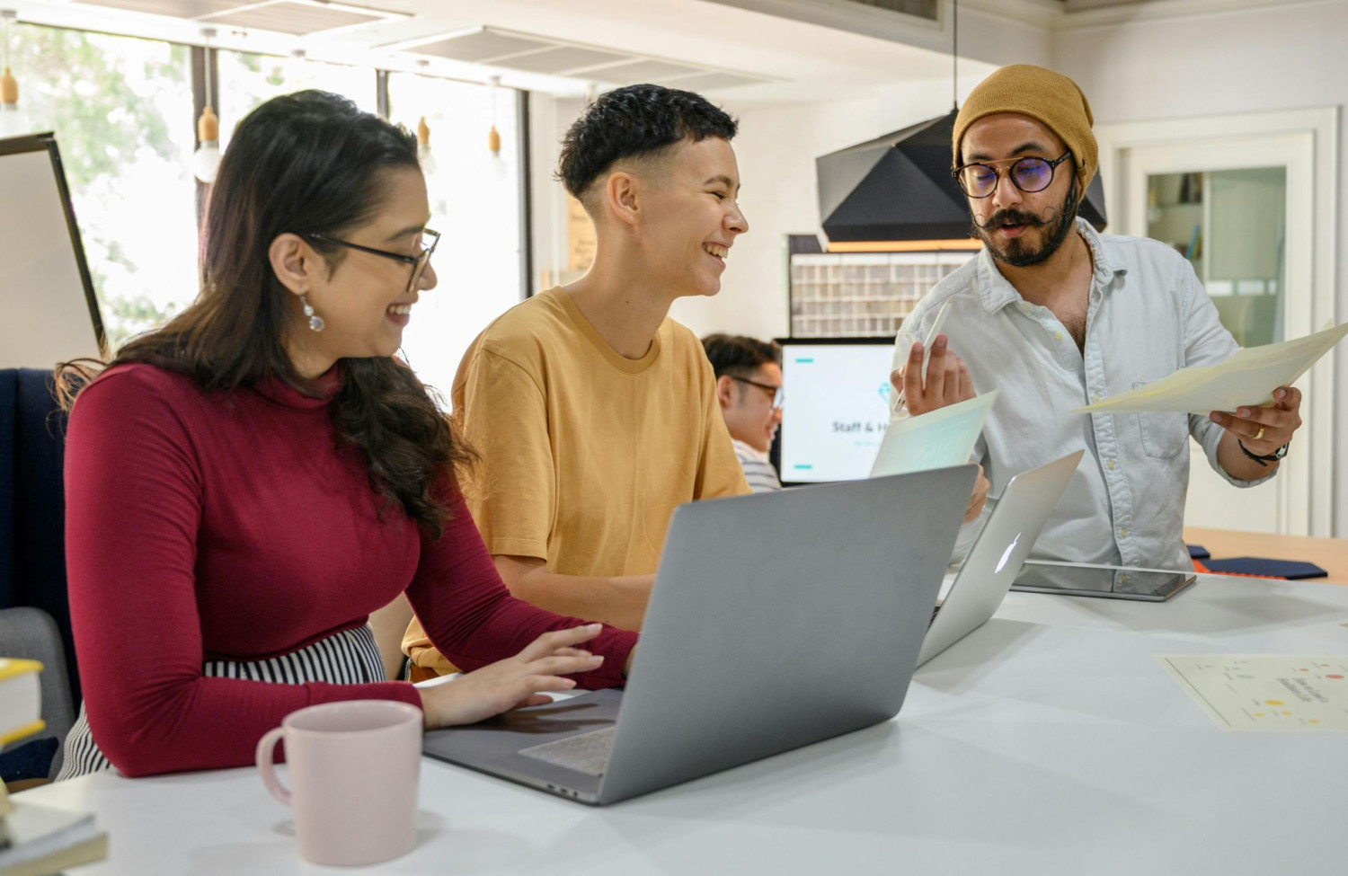 Drei Personen arbeiten gemeinsam an Laptops in modernem Büro.