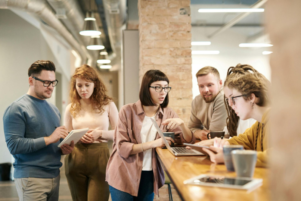 Sechs Personen arbeiten gemeinsam an Laptops und Tablets in einem modernen Büro.