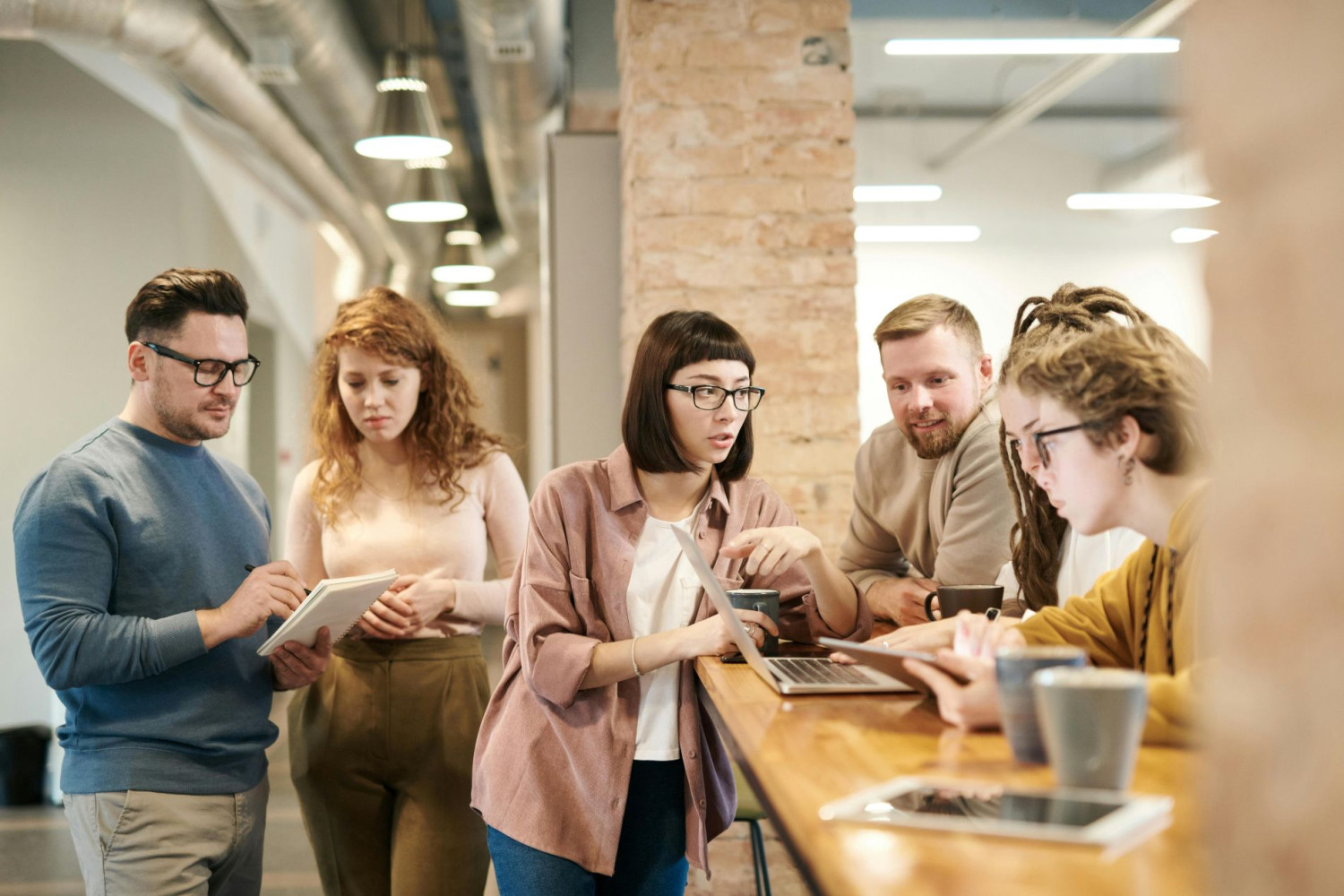 Sechs Personen arbeiten gemeinsam an Laptops und Tablets in einem modernen Büro.