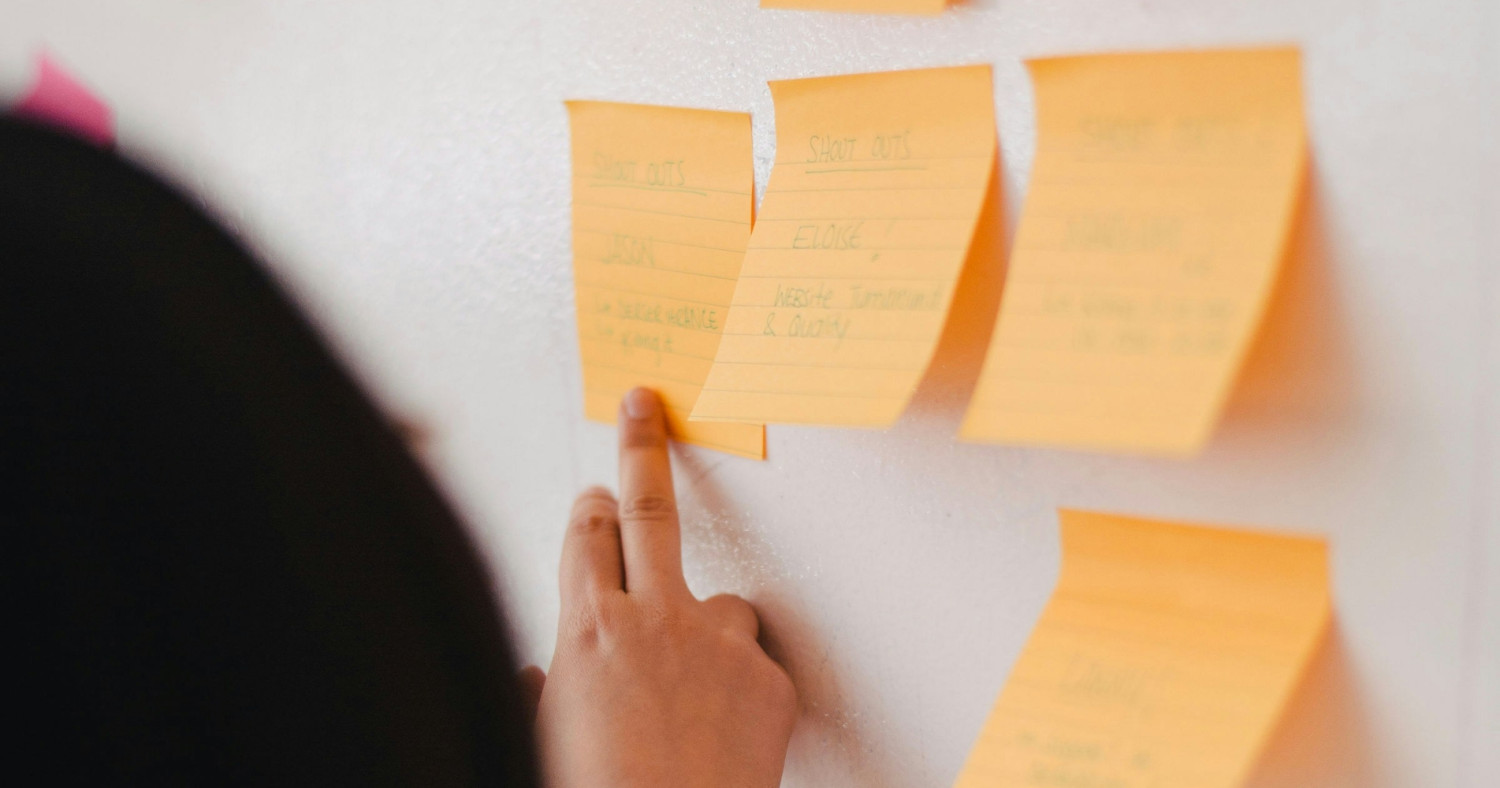 Eine Hand zeigt auf Postits an einer Wand.