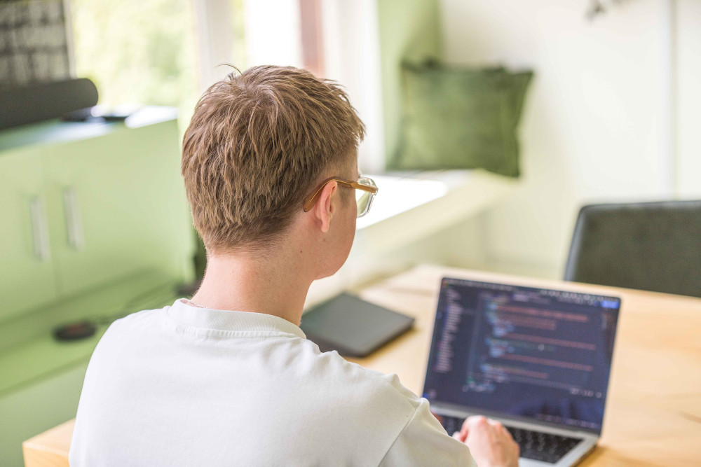 Eine Person sitzt an einem Tisch und arbeitet an einem Laptop.