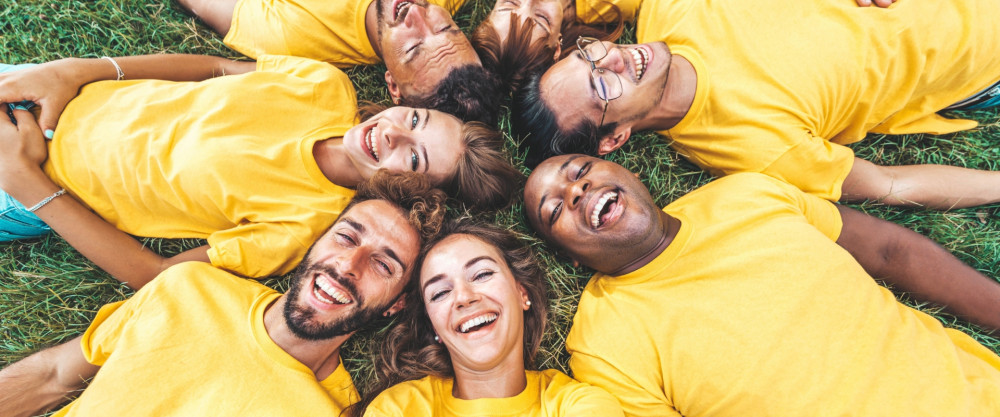Sieben Menschen liegen in einer Wiese und lachen