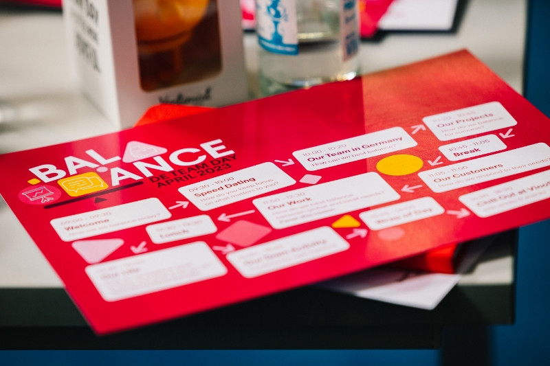 Ein roter Flyer des Balance DE Team Day von eBay liegt auf einem Tisch.