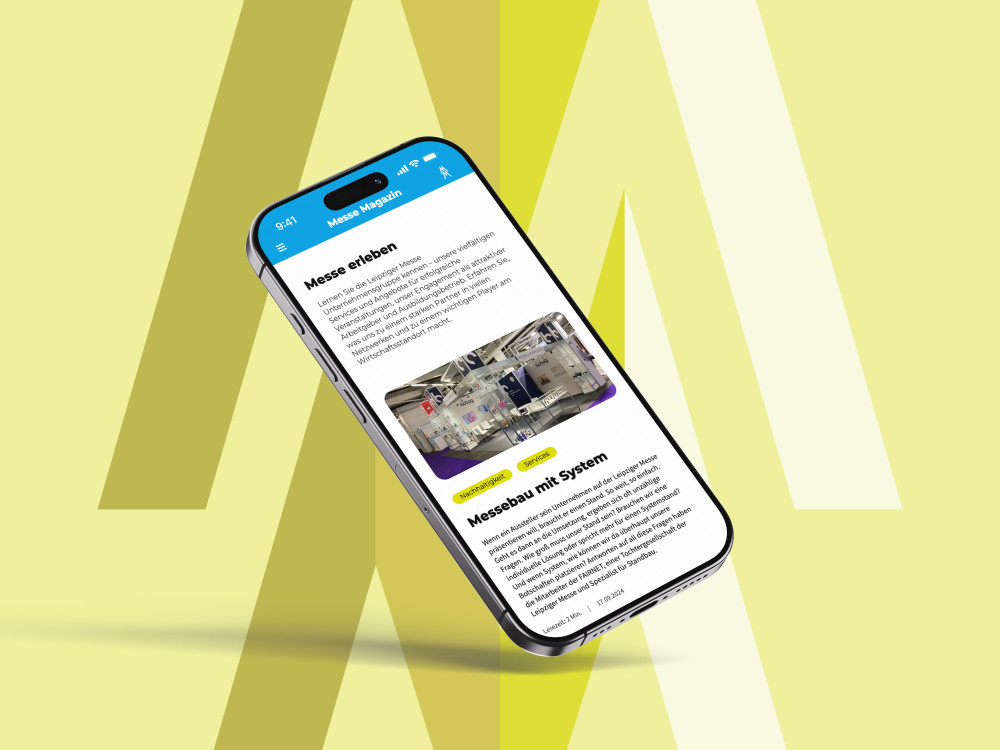 Ein Smartphone vorm Hintergrund des Doppel-M der Leipziger Messe. Auf dem Bildschirm ist die mobile Version des Messe Magazins geöffnet.