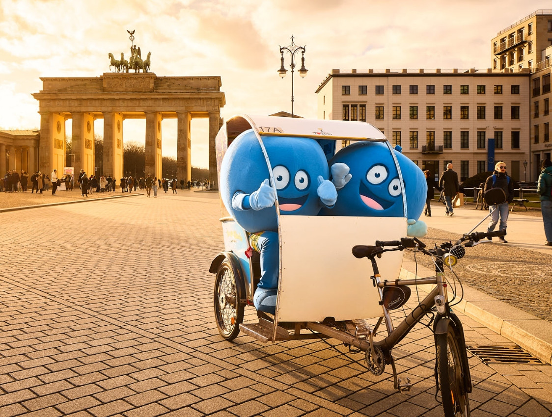 Zwei Pointies, die runden, blauen Maskottchen von PayBack, sitzen in einer Rikscha vor dem Brandenburger Tor in Berlin.