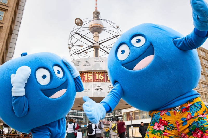 Zwei Pointies, die blauen, runden Maskottchen von PayBack, stehen vor der Berliner Weltzeituhr. Eines von ihnen trägt eine bunt geblümte Hose.