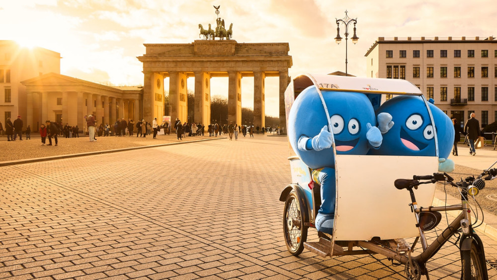 Zwei Pointies, die runden, blauen Maskottchen von PayBack, sitzen in einer Rikscha vor dem Brandenburger Tor in Berlin.