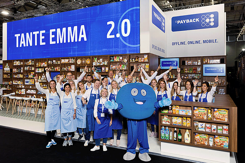 Payback-Stand auf einer Messe mit einem Pointee, dem runden, blauen Maskottchen von Payback, und dem Schild "Tante Emma 2.0" davor