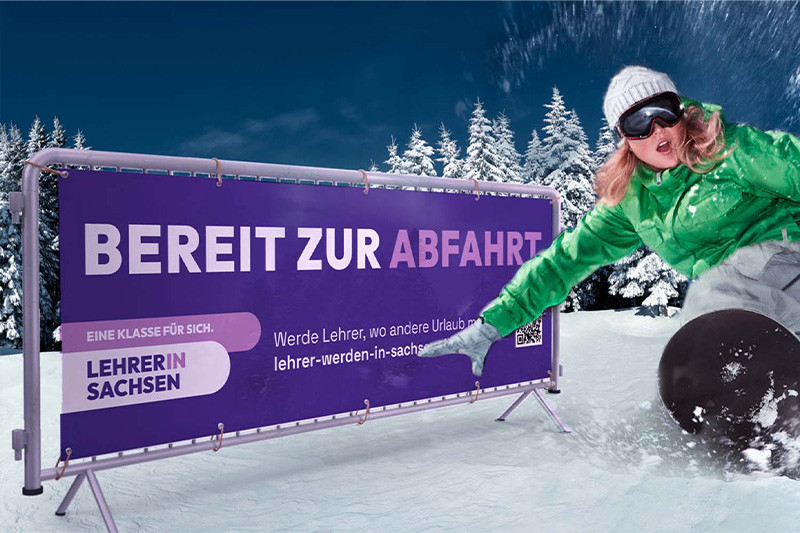 Plakat von "Eine Klasse für sich. Lehrer in Sachsen." auf einer Skipiste. Davor eine Frau, die Snowboard fährt.