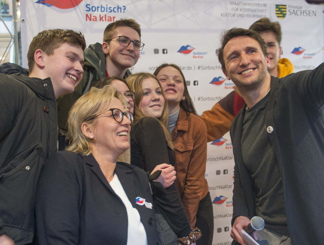 Mehrere Personen stehen vor einer Werbewand mit dem Logo der "Sorbisch? Na klar."-Kampagne und machen ein Selfie.