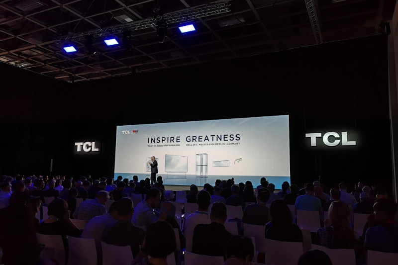 Das Messepublikum verfolgt eine Präsentation von TCL auf einer Bühne mit einer großen Leinwand.
