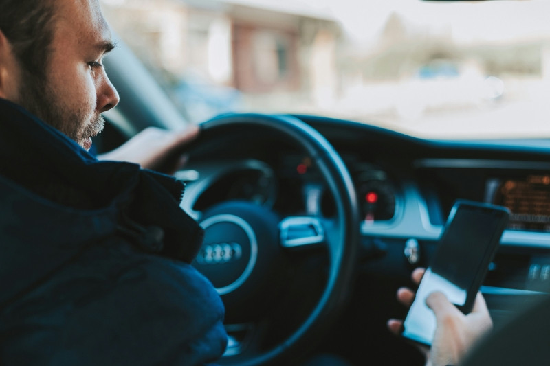 Ein Mann sitzt in einem Auto und hält ein Smartphone in der Hand.