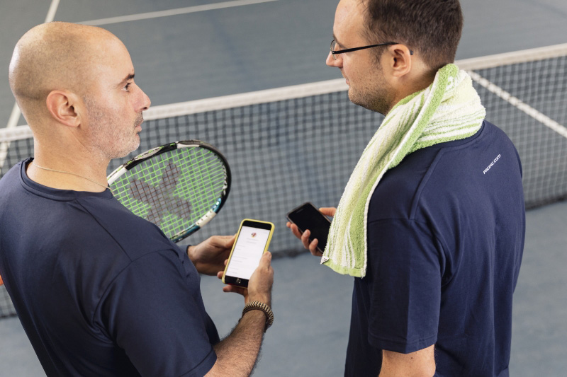 Ein Tenislehrer unterhält sich mit seinem Schüler mit einem Handy in der Hand.